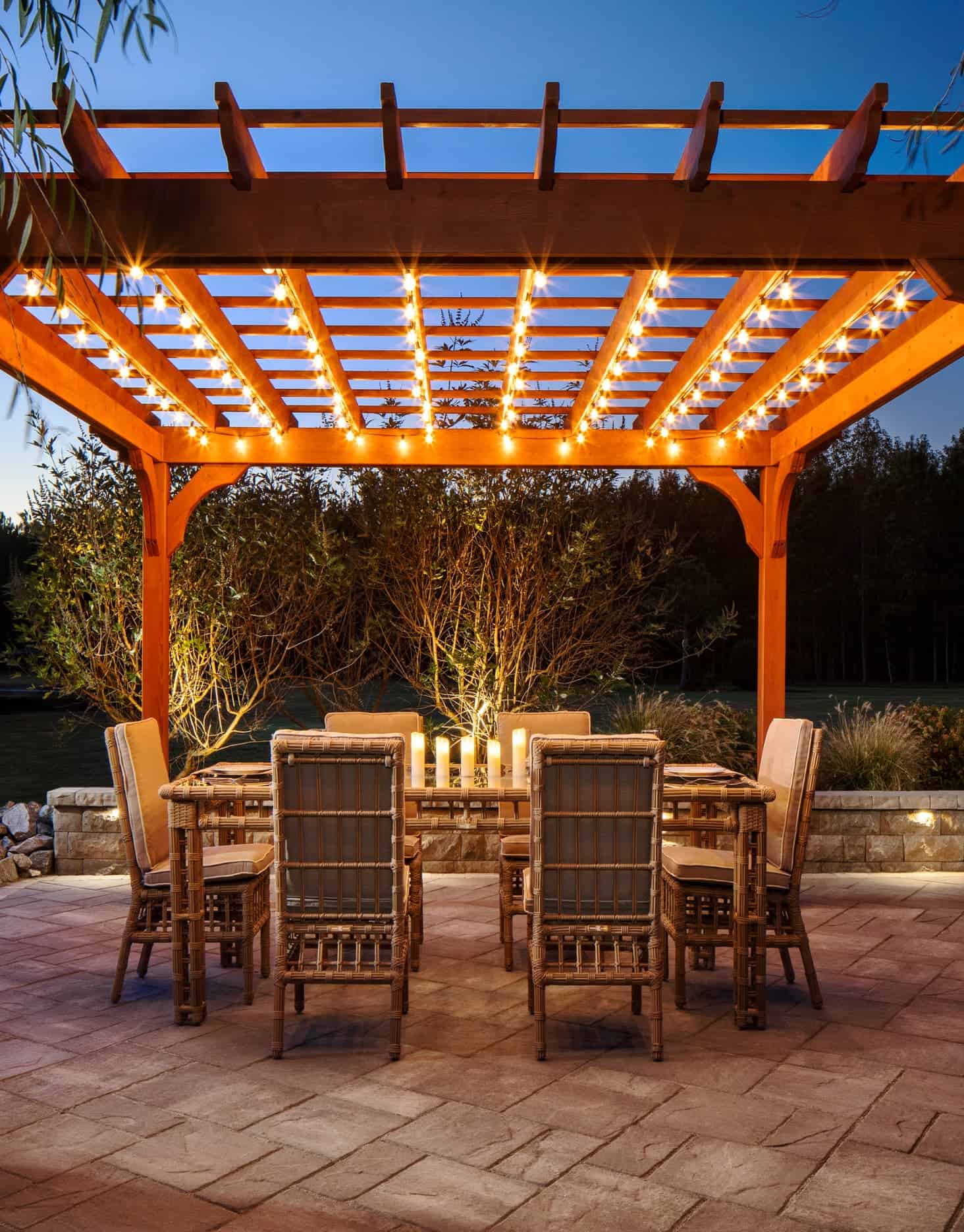 An outdoor dining space with a pergola and lights using Belgard products