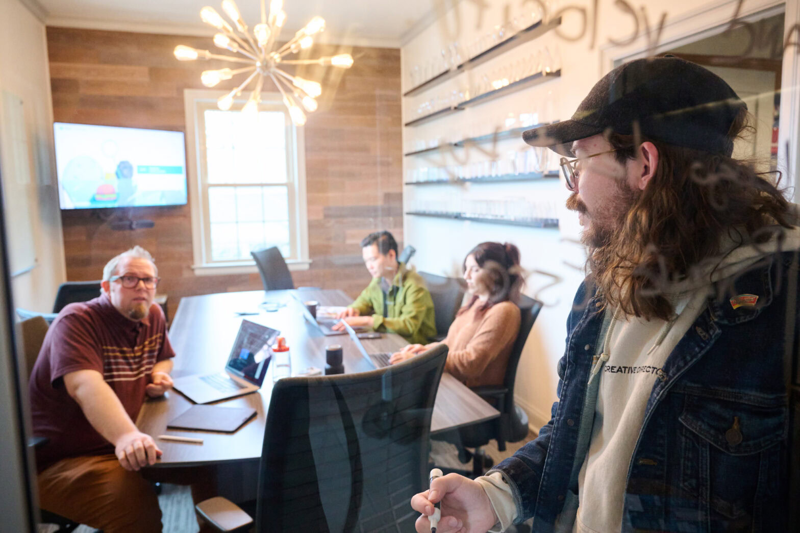 Four MESH employees gathered in the conference room. One is standing up and turned to talk to another employee who is sitting at the conference table. 