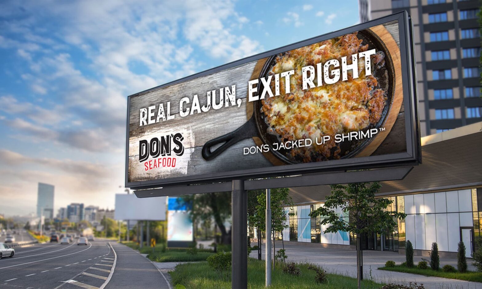 Billboard next to an interstate showing a cast iron pan filled with Don's Jacked Up Shrimp, captioned "Real Cajun, exit right".